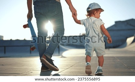 father and baby son at skatepark. happy family a kid dream concept. father son holding hands holding skateboard going to playground skatepark. father's day lifestyle concept