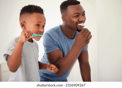 Father brushing his teeth with his child for oral hygiene, health and wellness in the bathroom. Dental, teaching and young African man doing his morning mouth routine with his boy kid at their home. - Shutterstock ID 2336909267