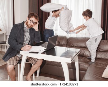 Father businessman try to work at the laptop from home while his children play around. Boys playing pillow fighting. Stressed father. Quarantine time. Stay at home concept. Freelancer