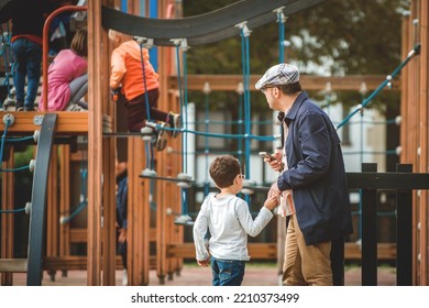 Father Busy With Smart Phone And Does Not Want To Play With Kid. Alone Child Boy. Dad Looks At His Phone And Does Not Follow Children In The Playground