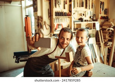 Father carpenter taking selfie with daughter in workshop - Powered by Shutterstock