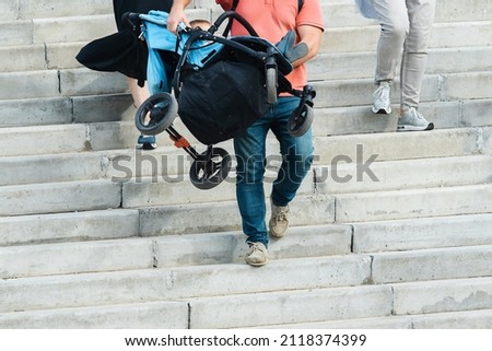 The father carries the baby carriage down the stairs. A man descends the concrete steps with a child in his arms. Lack of ramps in public places and city streets. unrecognizable person