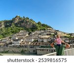 Father carries child piggyback on Gorica bridge in tourist town Berat in Albania, Europe. Footbridge crosses river Osum. UNESCO World Heritage Site with Ottoman architecture. City of thousand windows