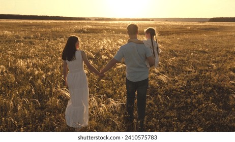 Father carries daughter blending with rustle of wind through ears of wheat. Father embraces held daughter and wife walks near wheat field. Father holds daughter in arms remained unwavering - Powered by Shutterstock