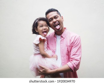 Father carry his daughter showing funny expression with their tongue out both wearing pink clothes