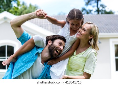 Father carrying daughter on shoulder besides woman in yard - Powered by Shutterstock