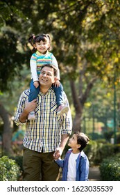 Father carrying daughter on shoulders and holding hands of his son at park