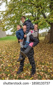 The Father Is Carrying Three Children. Father Carrying Childs Piggyback. The Father Plays With The Childrens On An Autumn Day