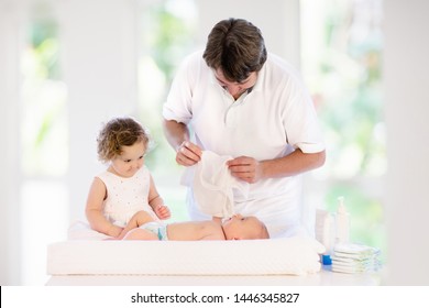 Father Changing Diaper To Baby Boy. Little Girl Helping Dad To Change Nappy Of Newborn Brother. Family In Kids Bedroom. Parent Taking Care Of Infant. Kid On Dressing Table On Towel After Bath.