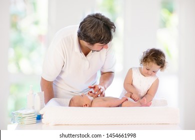 Father Changing Diaper To Baby Boy. Little Girl Helping Dad To Change Nappy Of Newborn Brother. Family In Kids Bedroom. Parent Taking Care Of Infant. Kid On Dressing Table On Towel After Bath.