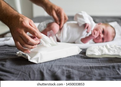 Father changing newborn baby's diaper on the bed with gray sheets and taking a wet wipe to clean the baby. No retouch, natural lighting. Man and child hygiene at home.