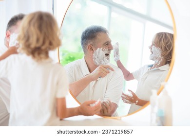 Father and child in bathroom looking in mirror. Dad shaving in white sunny bathroom, little boy playing with foam. Young man teaching son to shave. Father and kid bonding. - Powered by Shutterstock