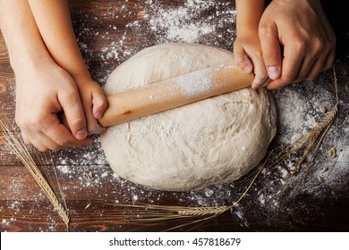 Father And Child Hands Making The Dough With Flour, Rolling Pin And Wheat Ears On Rustic Wooden Table Top View. Homemade Pastry For Bread Or Pizza. Bakery Background.