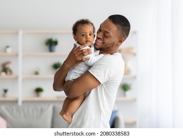 Father And Child. Happy Young Black Dad Embracing Cute Little Baby Boy While They Posing Together In Home Interior, Loving African American Daddy Looking At His Child And Smiling, Copy Space