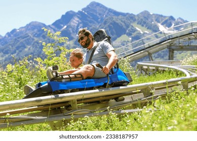 father and child having ride on summer toboggan called Rodelbahn rushing down the track. Beautiful mountains on background. Rosa Khutor resort, sochi, Russia