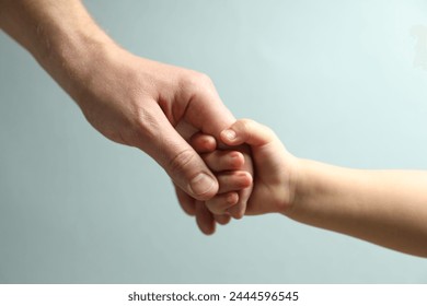 Father and child holding hands on light blue background, closeup - Powered by Shutterstock