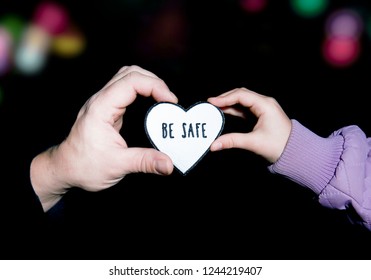 Father And Child Holding Heart-shaped Pedestrian Safety Reflector With Text Be Safe Outdoors With Dark Background And Bokeh City Street Lights