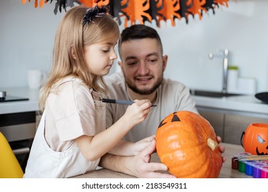 father and child paint a pumpkin making jack o lantern during Halloween celebration at home. focus on girl.