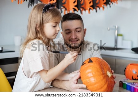 father and child paint a pumpkin making jack o lantern during Halloween celebration at home. focus on girl.