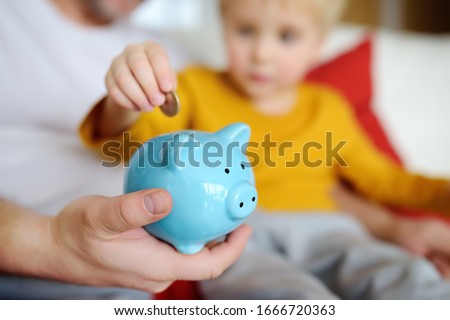 Father and child putting coin into piggy bank. Education of children in financial literacy. Money, cash, investment.