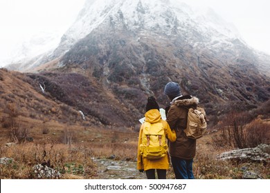 Father With Child Standing And Looking Map By The Mountain, Family Hike With Backpacks In Winter.