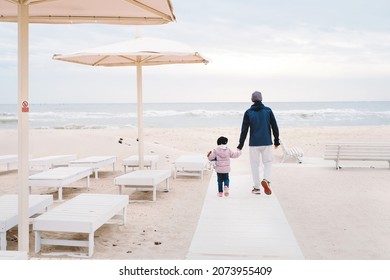 Father With Child Walking To The Beach In Autumn Fall Holding Hands, Offseason Sea. Fresh Air, Healthy Lifestyle, Family Spending Time Outdoors. Toddler Girl With Sporty Man On Empty Shore