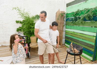 Father and children have a fun day in the backyard with a barbecue grill. The daughter blows bubbles while the father tends the fire and the son watches. - Powered by Shutterstock