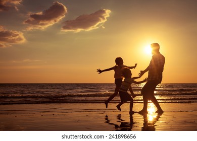 Father and children playing on the beach at the sunset time. Concept of friendly family.