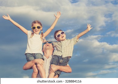 Father And Children Playing In The Park  At The Day Time. Concept Of Friendly Family. Picture Made On The Background Of Blue Sky.