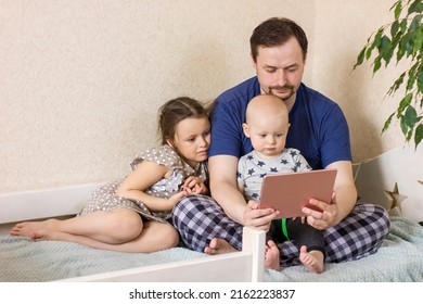 Father With Children Using Digital Tablet Computer Together At Home. Dad With Daughter And Son Watching Cartoons, Play Games Or Have Video Chat. Weekend Family Leisure Using Modern Technology.