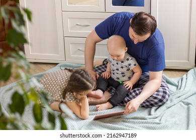 Father With Children Using Digital Tablet Computer Together At Home. Dad With Daughter And Son Watching Cartoons, Play Games Or Have Video Chat. Weekend Family Leisure Using Modern Technology.