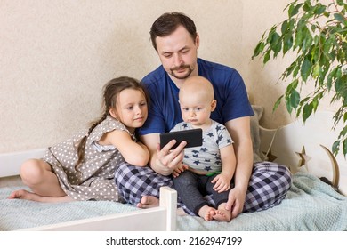 Father With Children Using Digital Tablet Computer Together At Home. Dad With Daughter And Son Watching Cartoons, Play Games Or Have Video Chat. Weekend Family Leisure Using Modern Technology.