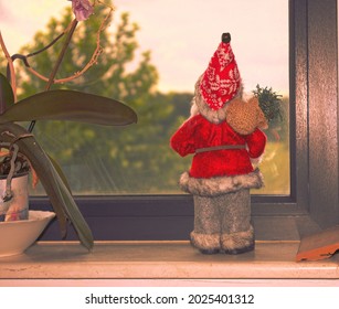 Father Christmas Doll With Bag Of Gifts Looking Through The Window. Solitude, Holidays In The Covid Era, Social Distancing And New Lockdown Concepts. 