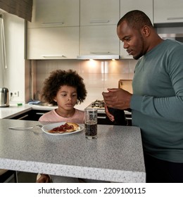 Father Closing Bottle Near His Little Son Having Lunch Or Dinner With Cola And Pizza At Table At Home Kitchen. Unhealthy Eating. Young Black Family Lifestyle And Relationship. Fatherhood And Parenting