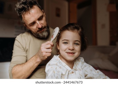 Father combing and braiding daughter's hair as part of bedtime routine. Single dad taking care of his daughter's hairstyle. - Powered by Shutterstock