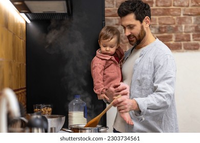 Father cooking meal holding toddler daughter in kitchenn. - Powered by Shutterstock