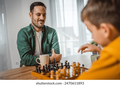 Father with cup of hot drink and son caucasian play chess together at home - Powered by Shutterstock