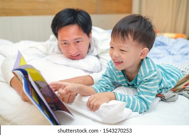 Father And Cute Little Asian 3 - 4 Years Old Toddler Boy Child Reading Bedtime Story Book, Lying In The Bed At Home, Dad And Son Spending Quality Time Together, Parents Reading To Child Concept