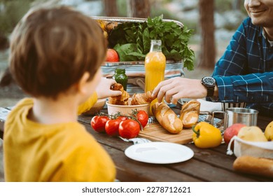 Niño de la escuela de papá padre que tiene un picnic en el campamento forestal con verduras, jugo, café y croissants. Cañón de madera con verduras orgánicas frescas rodeadas de panaderías