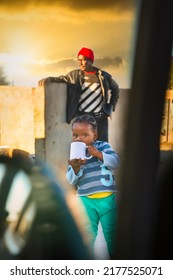 Father And Daughter In An African Village At Sunset, Girl With Braids Drinking Tea