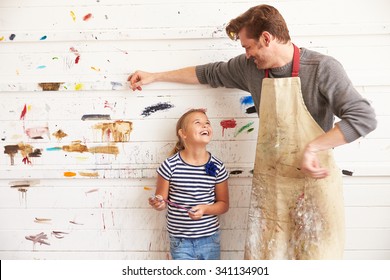 Father And Daughter Against Paint Covered Wall In Art Studio