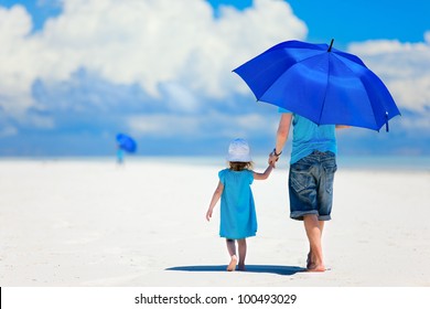 Father And Daughter At Beach With Umbrella To Hide From Sun