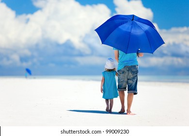 Father And Daughter At Beach With Umbrella To Hide From Sun