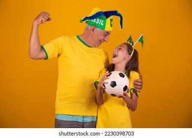 father and daughter brazilian fans on yellow background celebrating the brazil game. Father and daughter in brazil clothing holding soccer ball