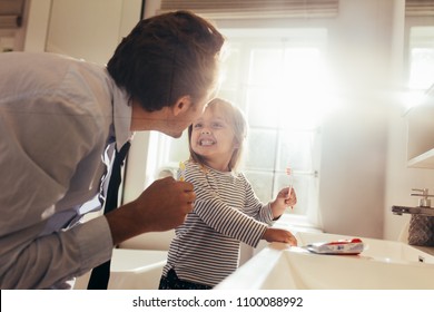 Father and daughter brushing teeth standing in bathroom and looking at each other. Man teaching his daughter how to brush teeth.