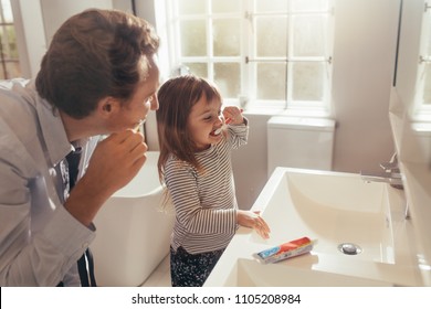Father and daughter brushing teeth standing in bathroom. Man teaching his daughter how to brush teeth.