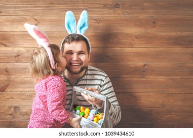 Father And Daughter In Bunny Ears With Colorful Eggs In Busket. Easter Day. Modern Family Preparing For Easter. Kids Painting Eggs On Wooden Background. Having Fun On Easter Egg Hunt. 