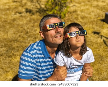 Father and daughter, family viewing solar eclipse with special glasses in a park.