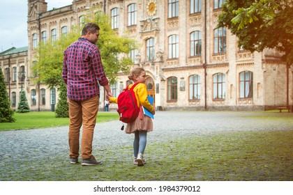 Father And Daughter Go Hand In Hand. Back To School. Dad And Kid Girl Of Primary School With Bag And Books. Parent Takes The Child To Lesson On First Day Of Fall Outdoors The Street. Happy Pupil.