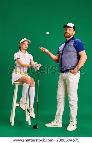 Father and daughter have fun on golf court. Dad, man and girl, teenager dressed like golf players posing on green background. Concept of parenthood, hobby, recreation, healthy and active lifestyle.